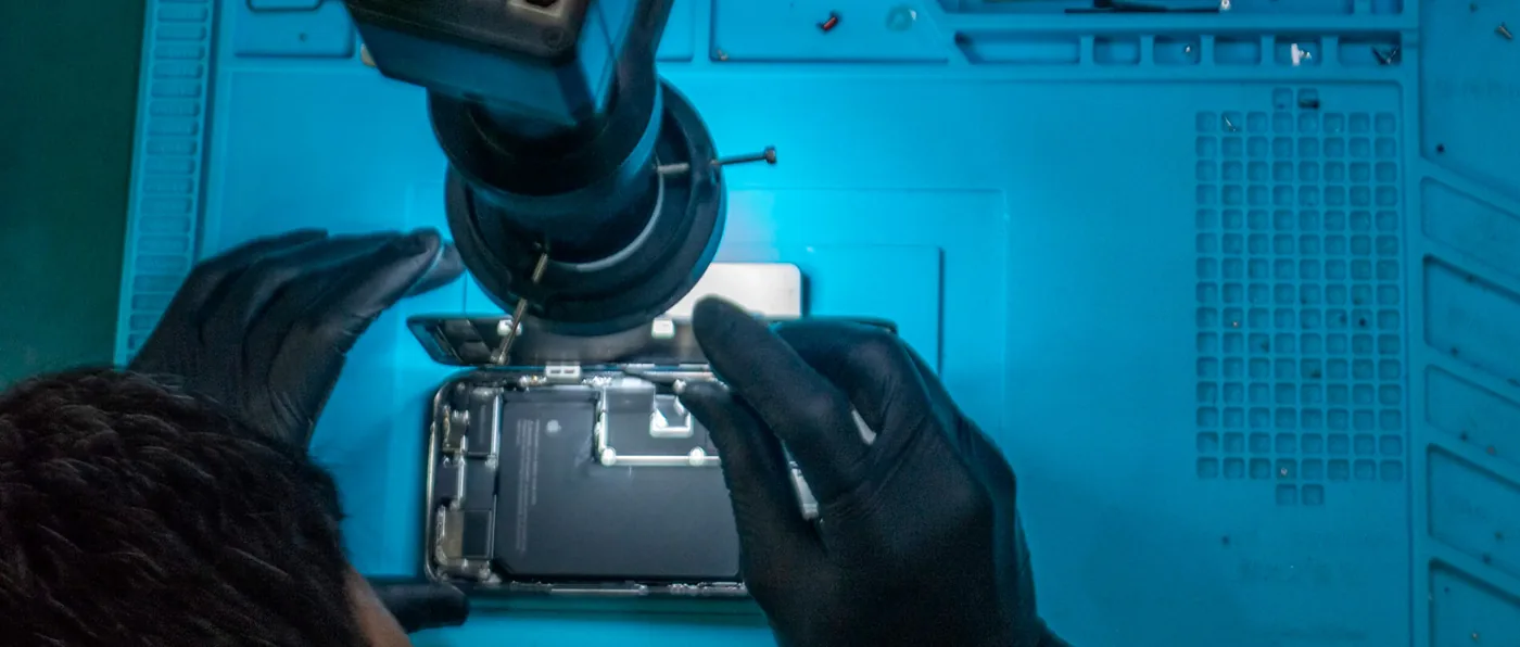 Técnico da iTelas fazendo reparo de placa Apple sob microscópio na bancada